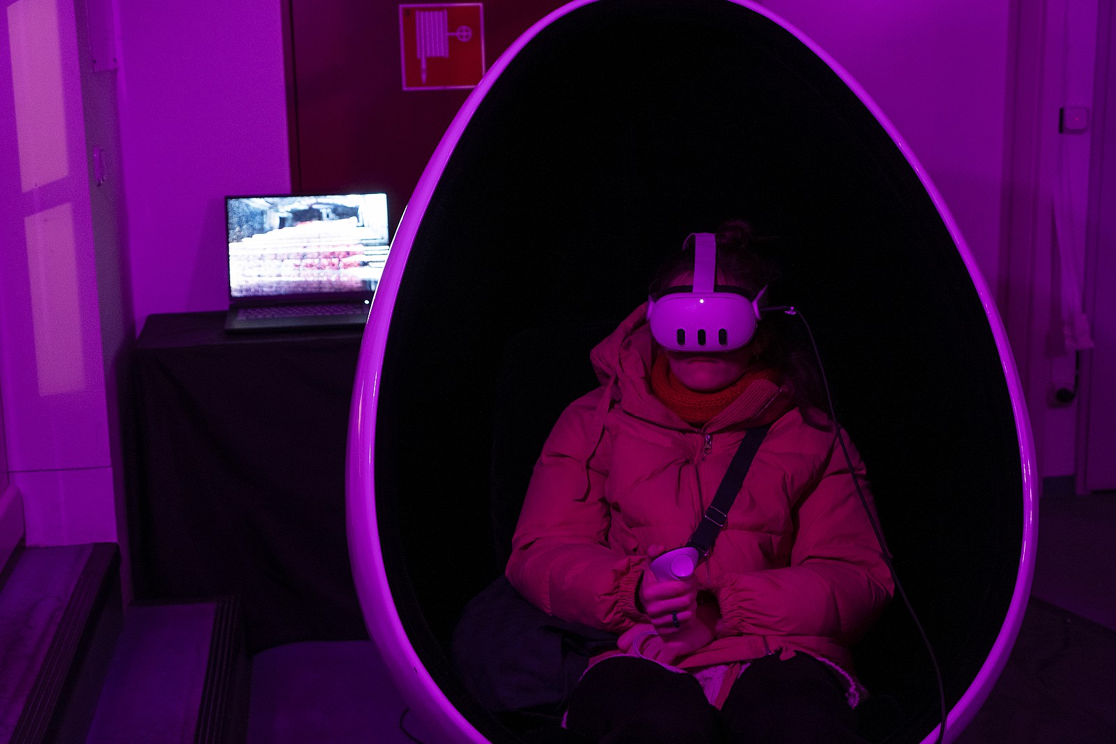 Frau sitzt in einem Ei, hält einen Controller in der Hand