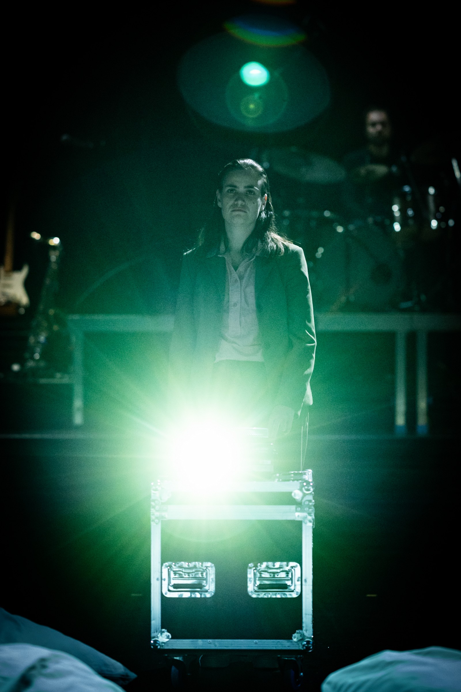 Eine Person im Anzug steht hinter einem grell leuchtenden Scheinwerferkasten, während im Hintergrund ein Schlagzeuger zu sehen ist.